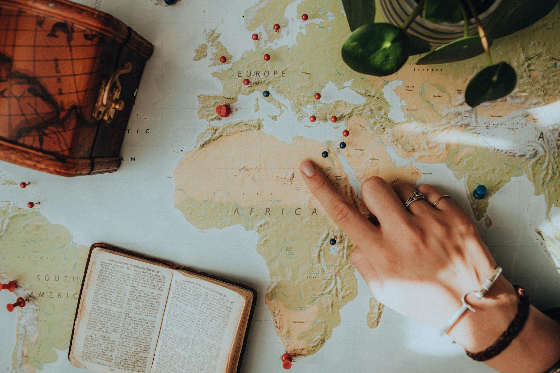 Close-up of a hand pointing on a map, surrounded by travel essentials.
