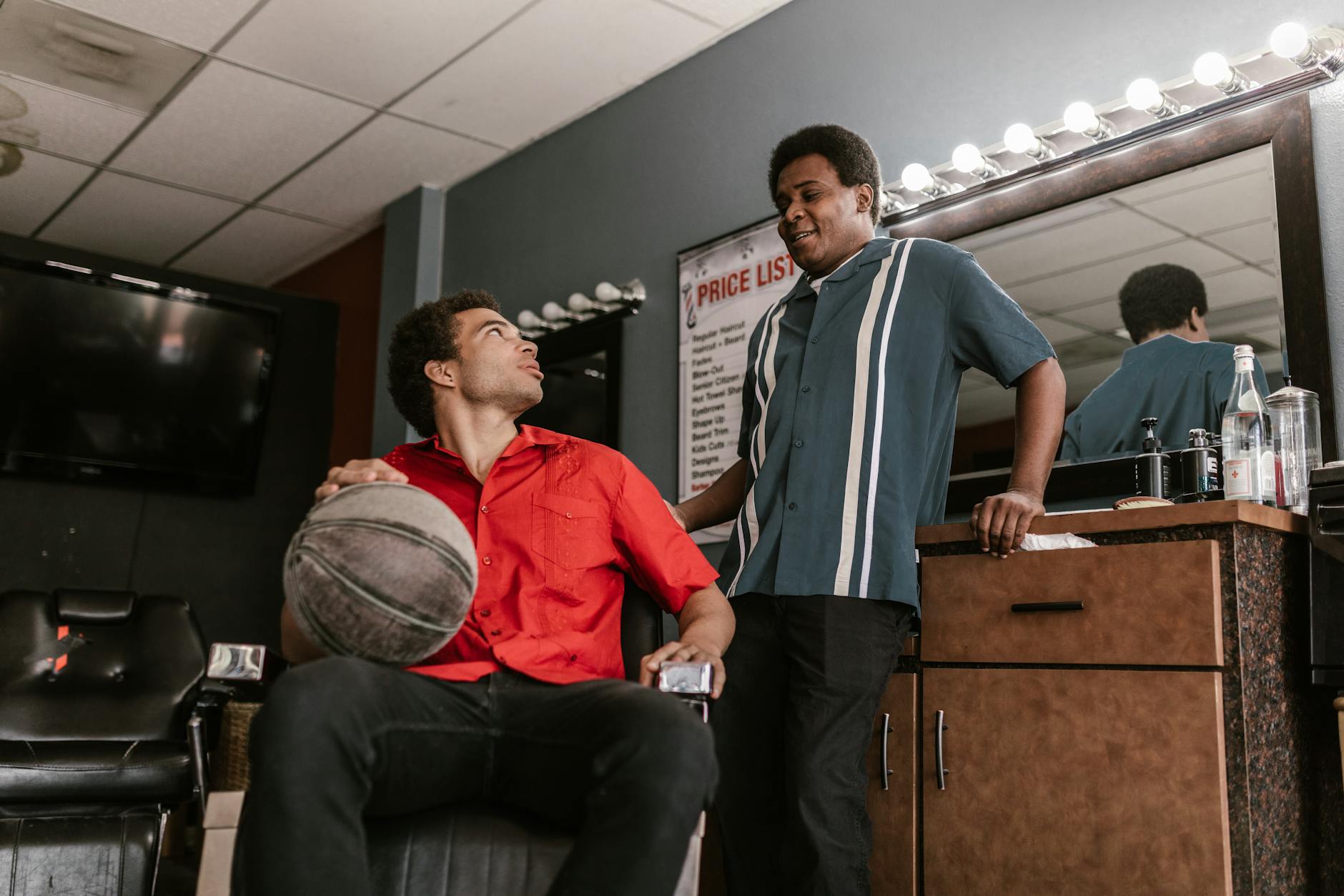 Two men in a barbershop having a relaxed conversation, one holding a basketball.